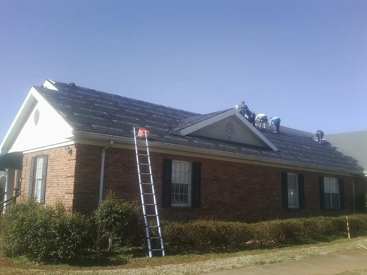 Crew tearing shingles off a brick ranch roof with a ladder set — Metal Roof Repair work by our crew in Fredonia