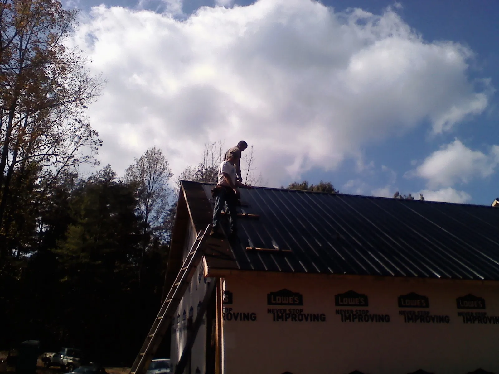 Roofer fastening dark metal panels high against a cloudy sky, from a Roof Inspection job in Fredonia